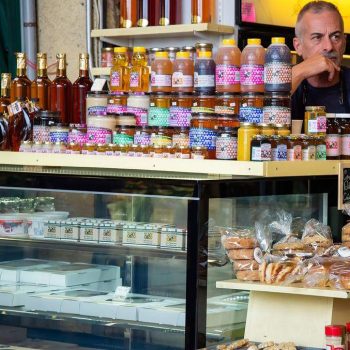 Muškarac stoji iza tezge sa teglama meda, džemova i pekarskim proizvodima