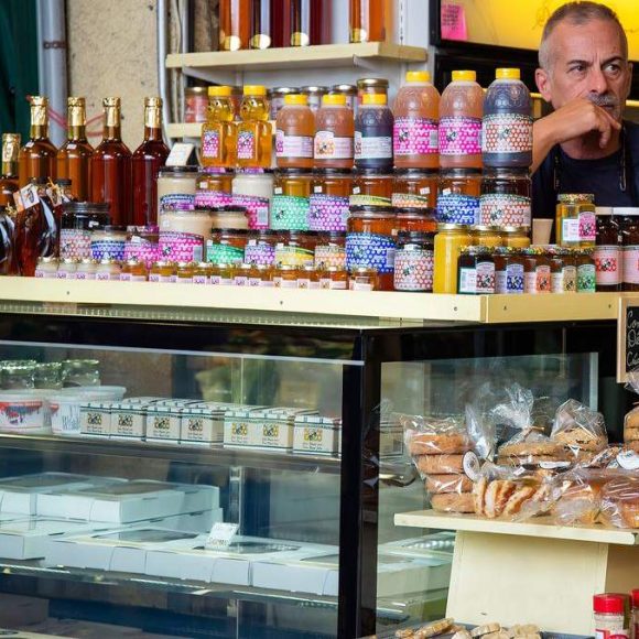 Muškarac stoji iza tezge sa teglama meda, džemova i pekarskim proizvodima